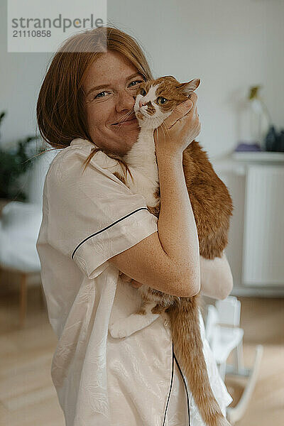 Happy woman embracing cat at home