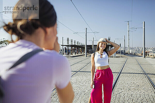 Woman photographing smiling friend on tram tracks