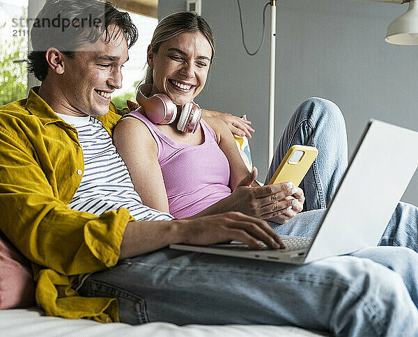 Smiling woman sharing smart phone with boyfriend sitting at home