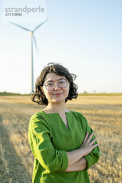 Confident engineer standing with arms crossed at wind farm