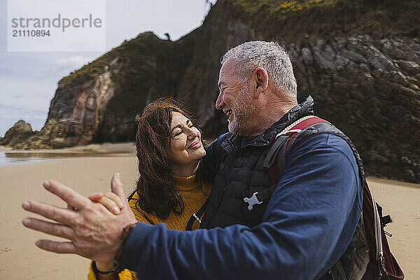 Happy elderly couple holding hands and dancing on beach