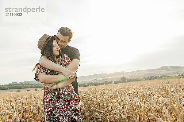 Young man embracing girlfriend in spikelet field