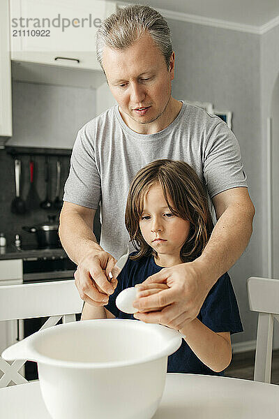 Father with son holding egg near bowl in kitchen