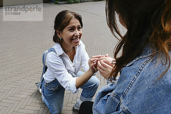 Happy woman with ring proposing to girlfriend at footpath