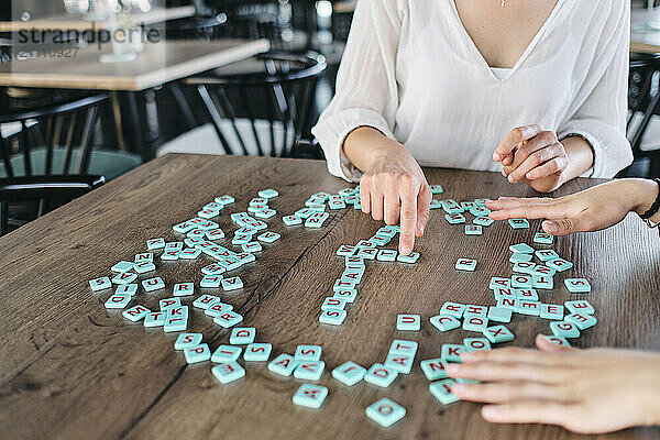 Hands of two young women playing word game at cafe table