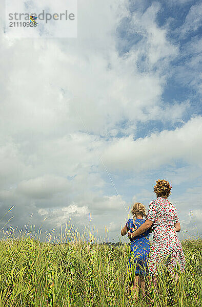 Mother teaching daughter to fly kite in agricultural field