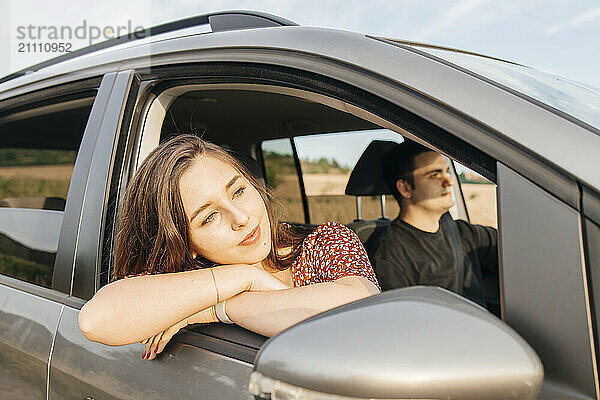 Thoughtful young woman leaning on car window during road trip with boyfriend