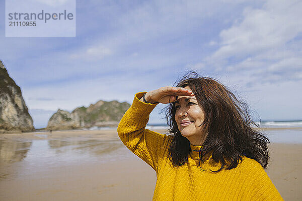 Smiling senior woman shielding eyes at beach