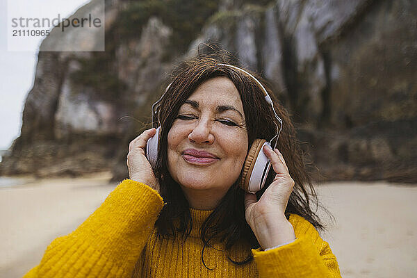 Carefree senior woman with eyes closed listening to music on beach