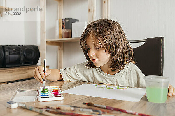 Boy using watercolors and painting on paper at home