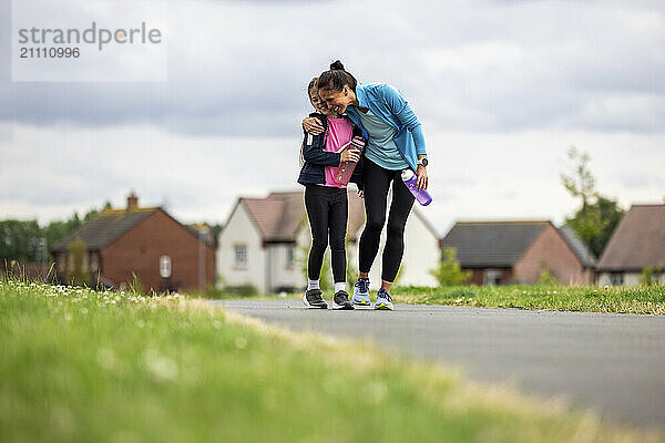 Happy woman embracing daughter walking on footpath