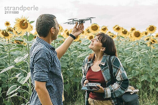 Smiling woman with man flying drone at sunflower field