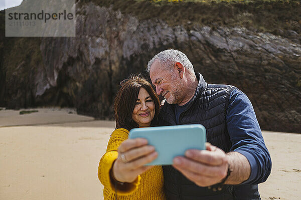 Happy senior couple taking selfie through smart phone at beach