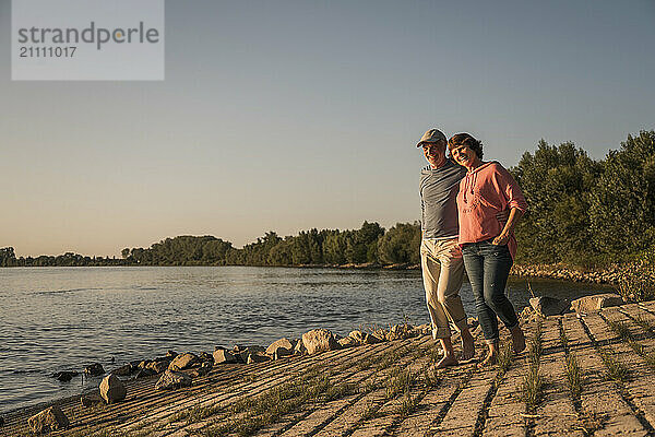 Happy senior couple walking at riverbank on sunny day