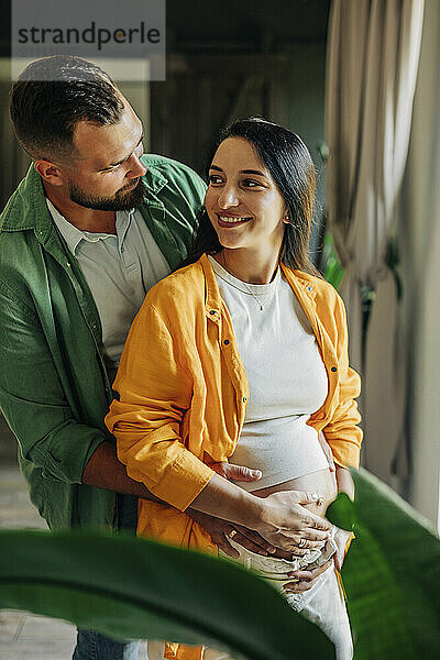 Husband embracing pregnant wife at home