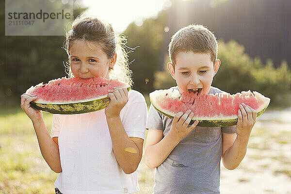 Brother and sister enjoying slices of watermelon in public park