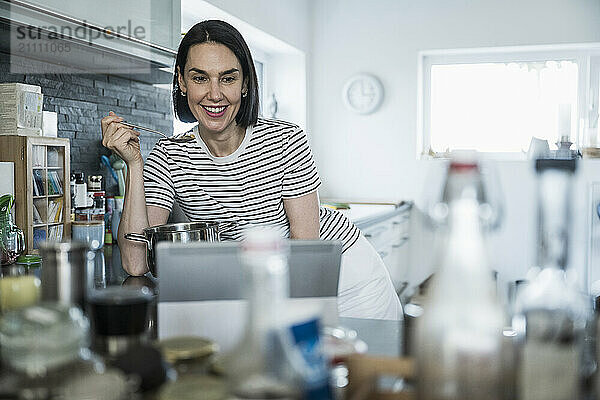 Woman holding spoon and tasting food in kitchen at home