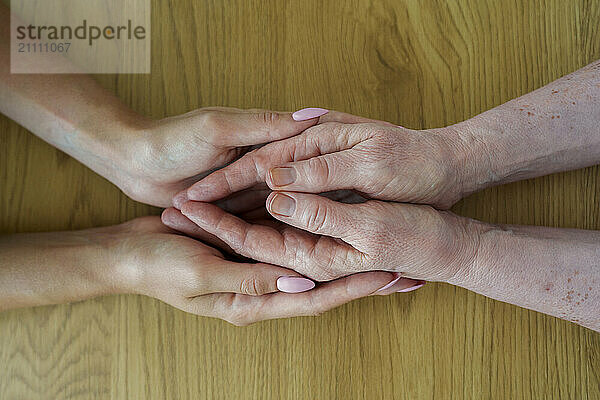 Woman holding hands with senior mother at table