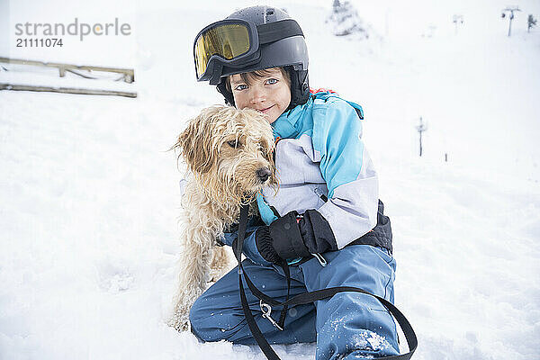 Smiling boy with doodle dog on snow in winter