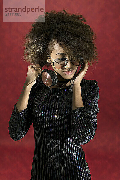 Fashionable young woman listening to music against red background