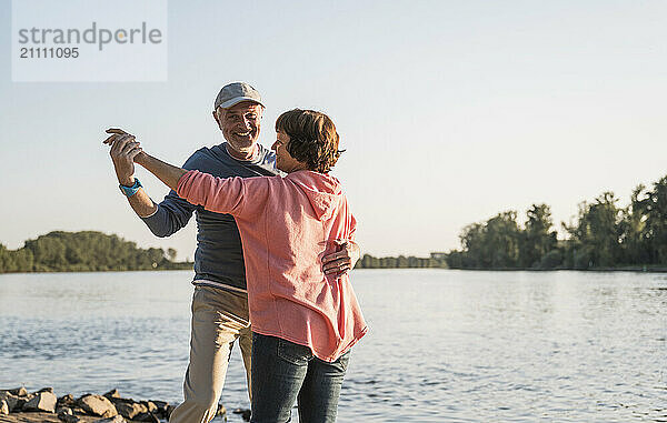 Affectionate couple dancing together near river on sunny day