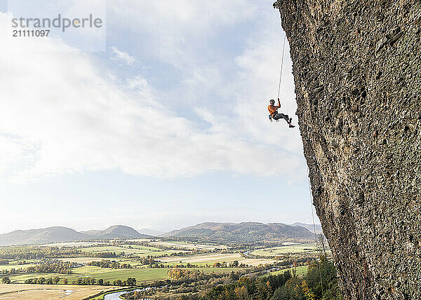 Climber on rocky wall under cloudy sky