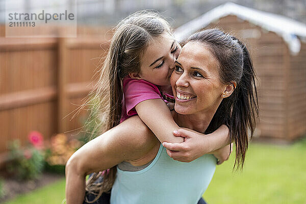 Smiling woman piggybacking daughter in back yard