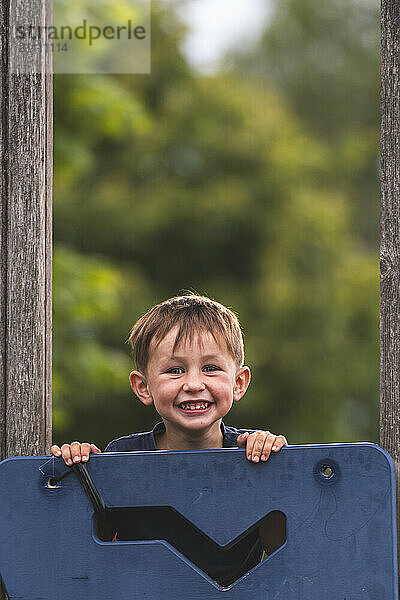 Cute boy standing behind play equipment at playground