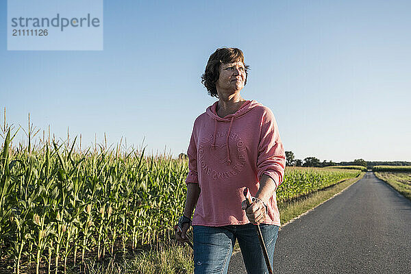 Senior woman walking on road near green field