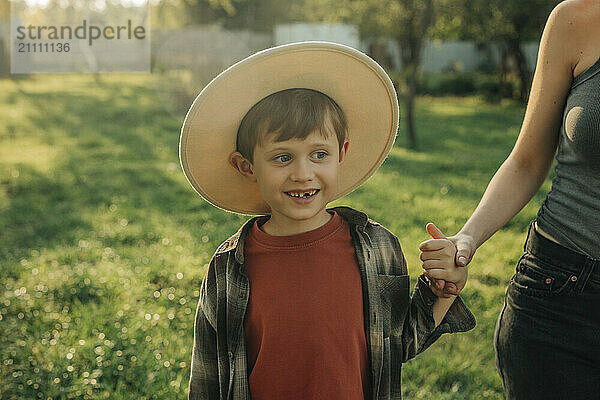 Cute boy wearing hat and holding mother's hand in farm