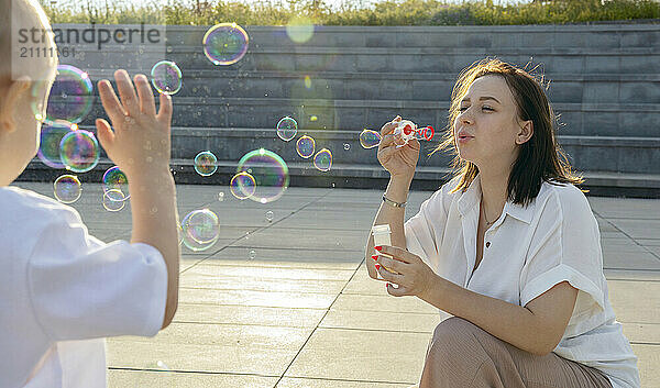 A dark-haired woman blows bubbles with her son.