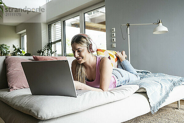 Smiling woman listening to music lying on sofa at home