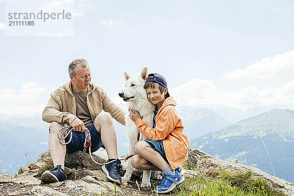 Father and son sitting with dog on mountain