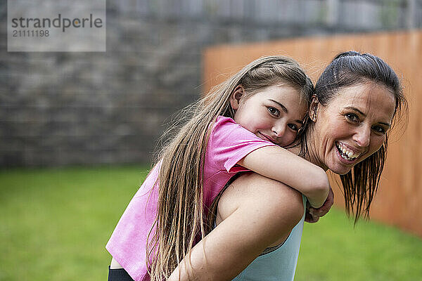 Happy woman piggybacking daughter in back yard