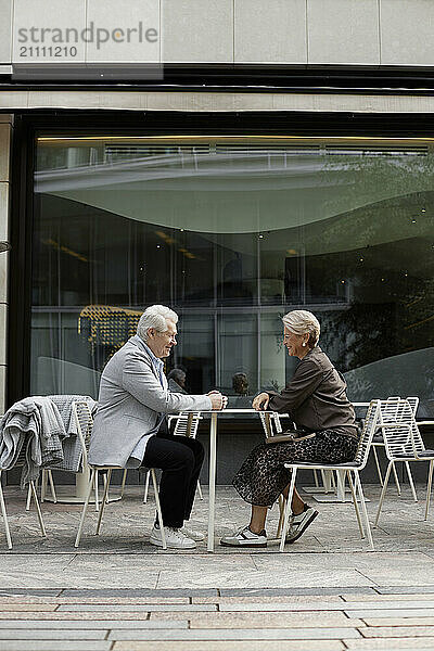 Senior man and woman sitting near table at sidewalk cafe