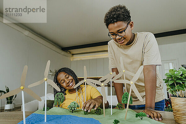 Happy siblings making wind turbine project at table in living room