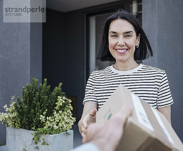 Cheerful woman receiving package standing outside house