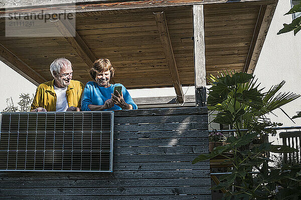 Senior man with woman using smart phone near solar panel at balcony