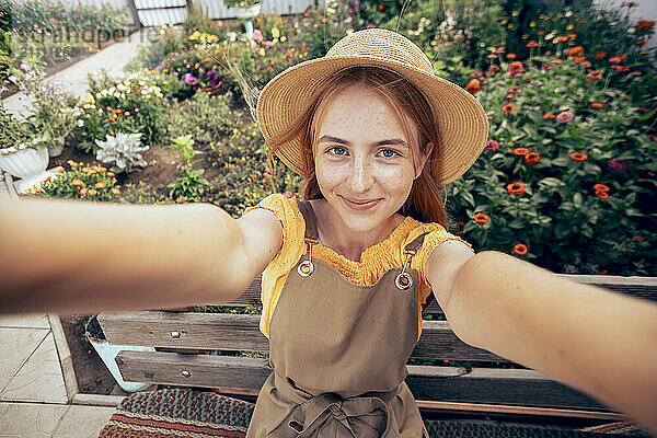 Happy girl wearing overalls taking selfie in garden