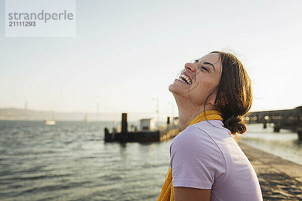 Happy young woman laughing at the waterfront at promenade