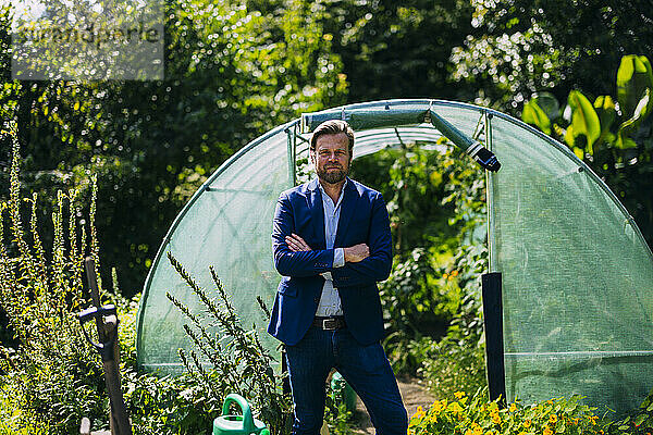 Smiling businessman standing with arms crossed near greenhouse