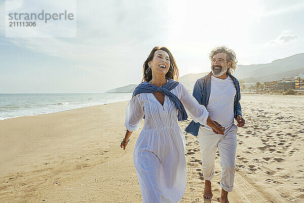 Happy senior couple holding hands and running at beach