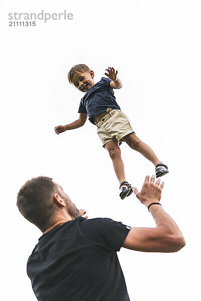 Carefree boy in mid-air playing with father under clear sky