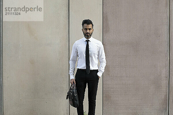 Businessman with hand in pocket standing in front of wall