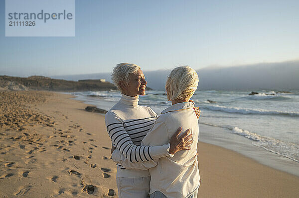 Happy woman embracing daughter standing on beach at sunny day