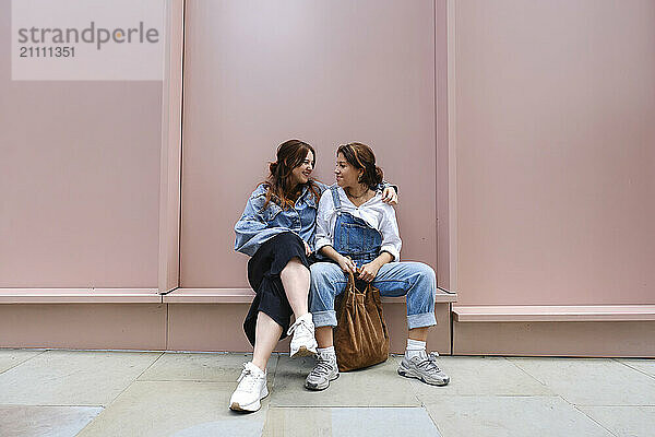 Happy gay couple sitting in front of wall at sidewalk