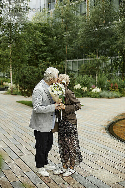 Senior man holding bouquet and kissing woman at street