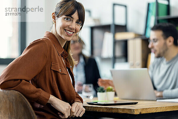 Smiling young businesswoman sitting near table at office