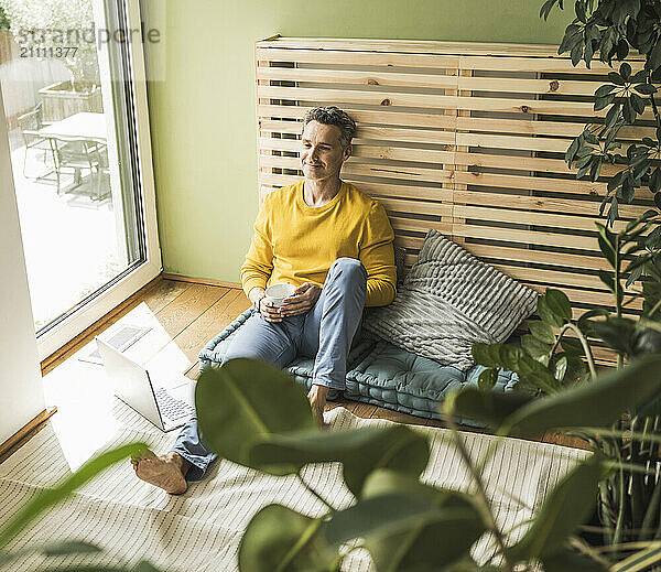 Portrait of man sitting on mattress in front of laptop