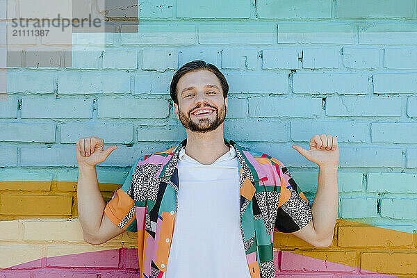 Happy man gesturing thumbs up in front of colored wall